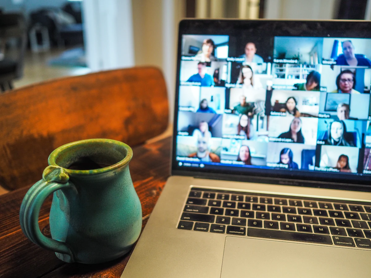 Laptop mit einer Videokonferenz und vielen Teilnehmenden, daneben eine Kaffeetasse